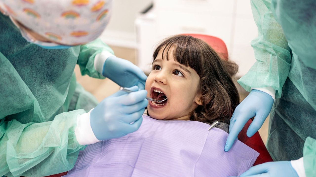 Dentista avaliando boca de paciente criança em consultório odontológico