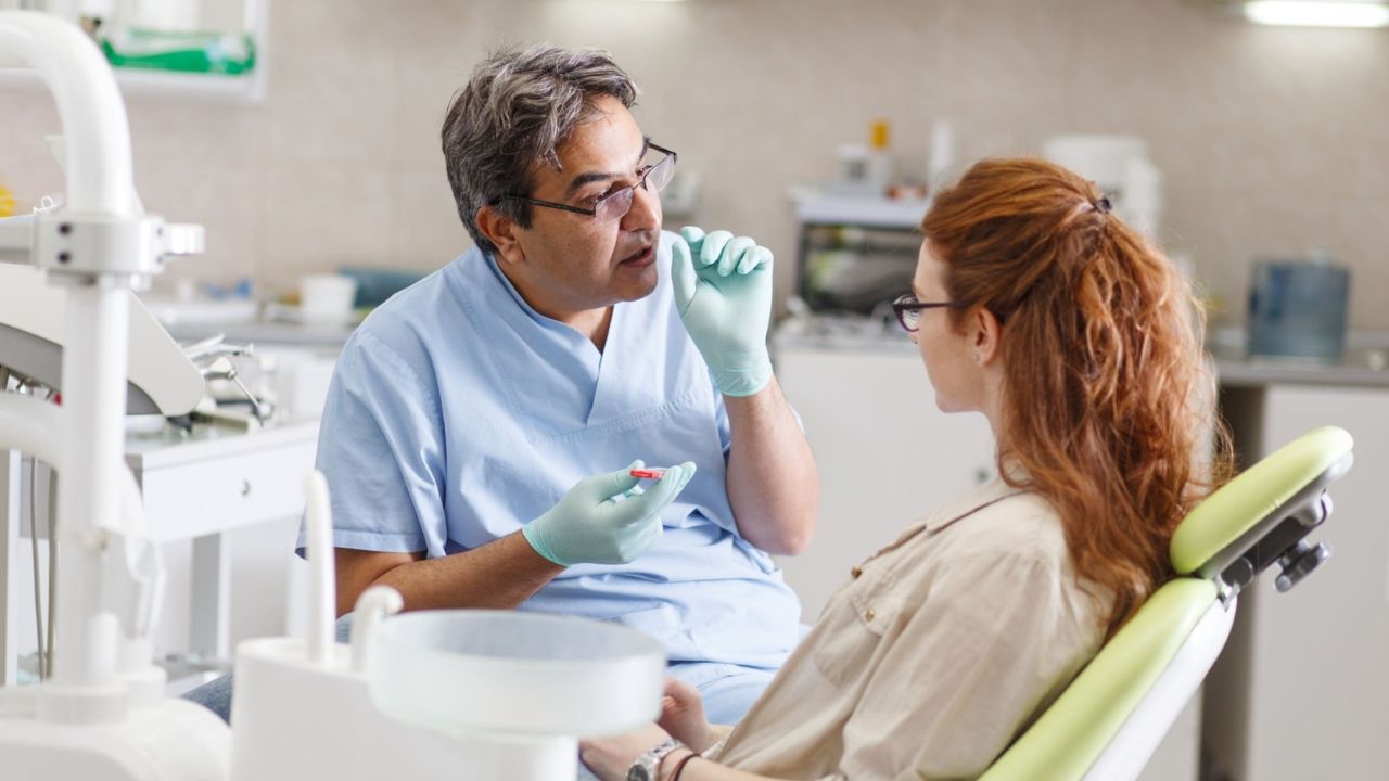 Paciente mulher em maca de consultório odontológico recebendo orientações do dentista para retração gengival 