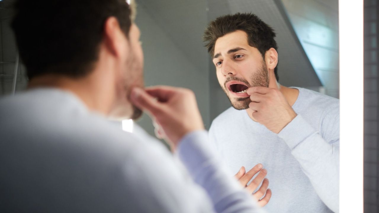 Homem se olhando no espelho enquanto cutuca local da arcada dentária em que está separador de dentes