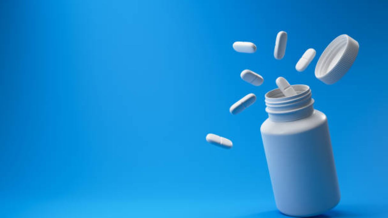 Pílulas brancas de nimesulida e recipiente médico plástico em um fundo azul.