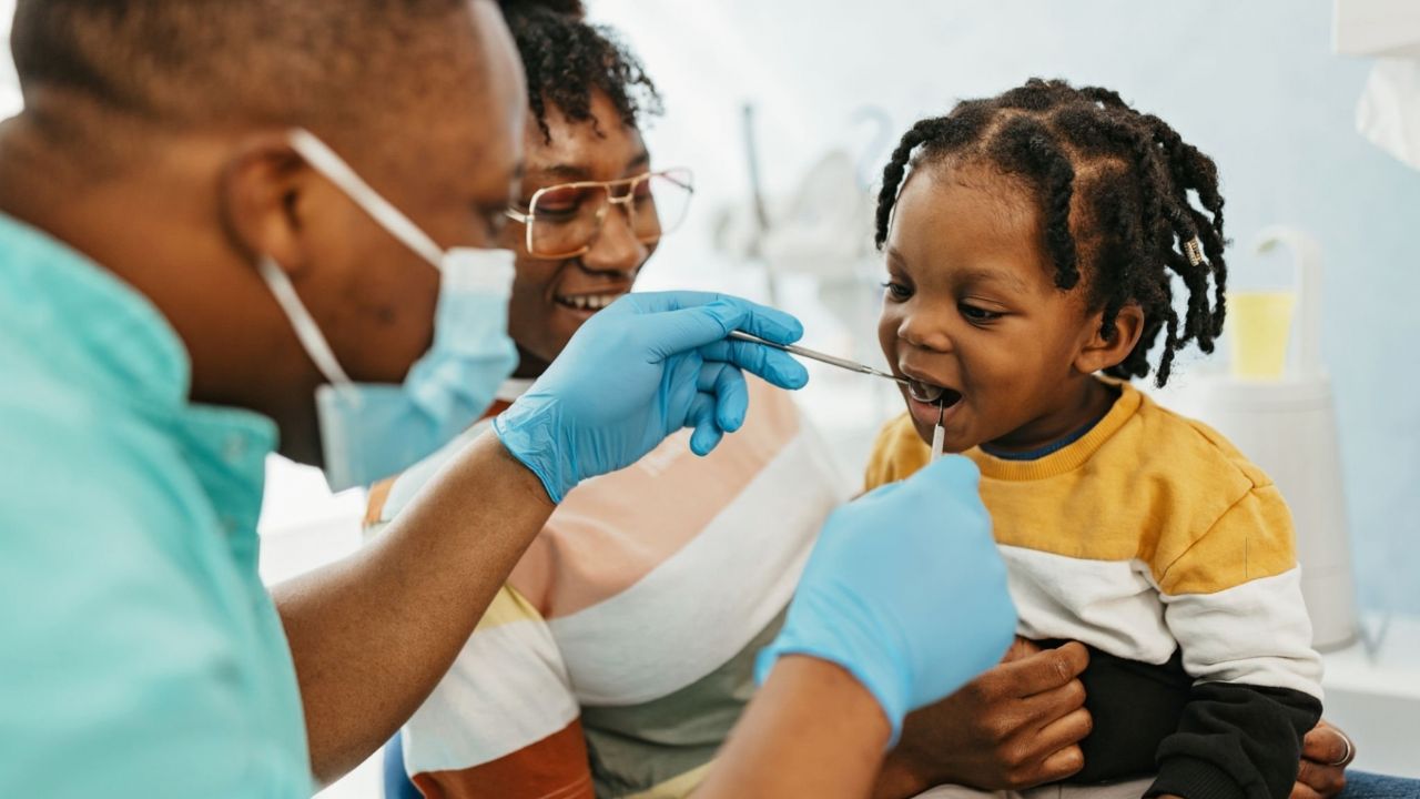 Dentista examinando boca de criança na presença de sua mãe