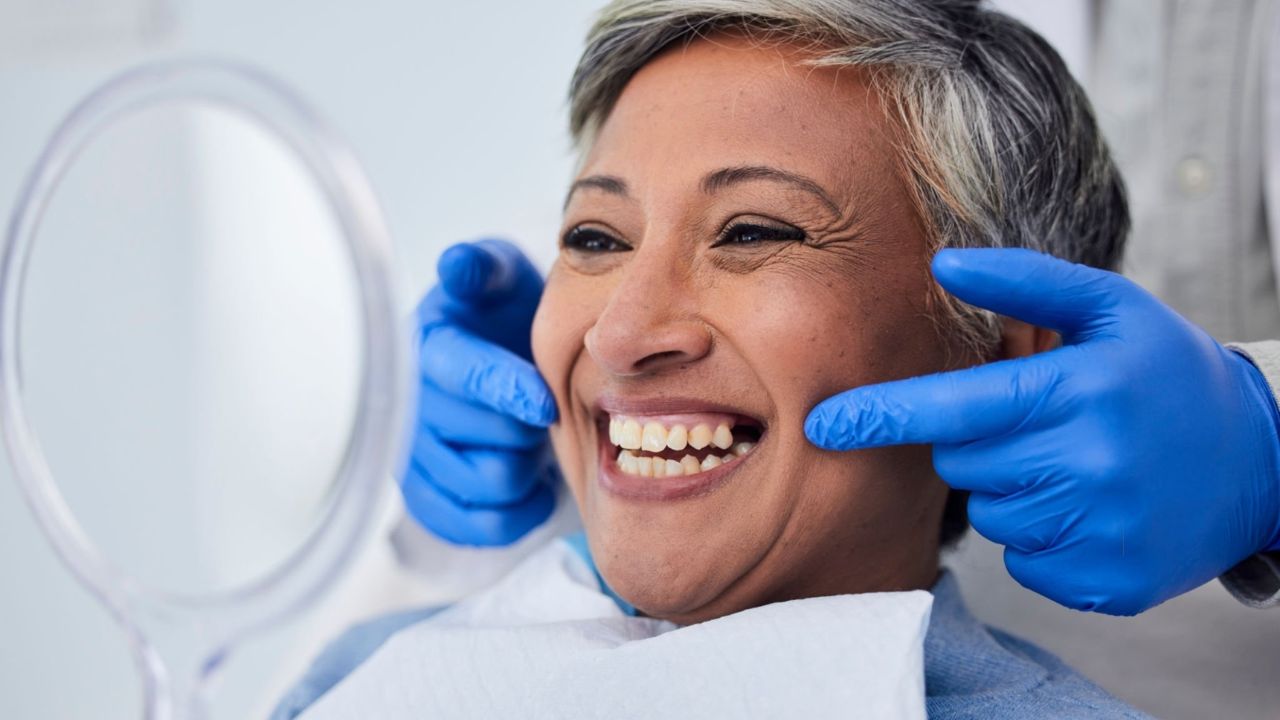 Mulher sorrindo se vendo em espelho de dentista depois de colocação de prótese dentária fixa superior