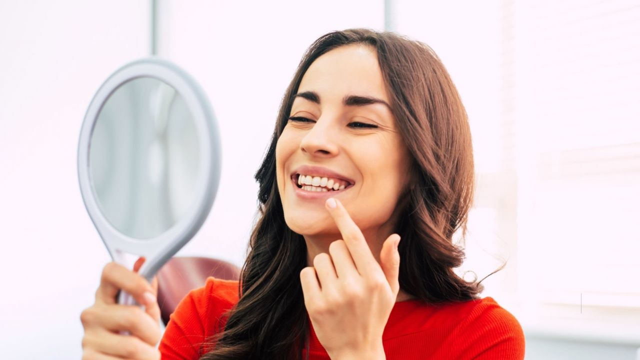 Paciente mulher olhando sorriso no espelho após colocação de lente de contato dental