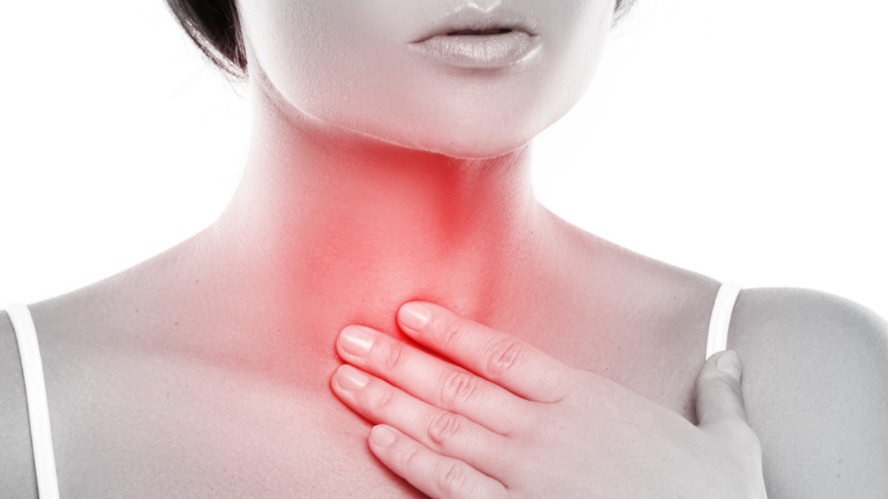 Uma imagem de uma mulher tocando o pescoço, próximo a região da garganta, como se estivesse sentindo dor.