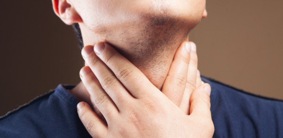 Um homem segurando a garganta, aparentemente com dores, sintoma de HPV na garganta,