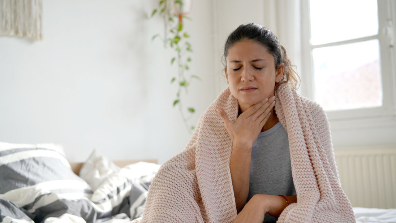 Uma mulher enrolada em cobertor sentindo dores na garganta, possível sintoma de câncer na língua.