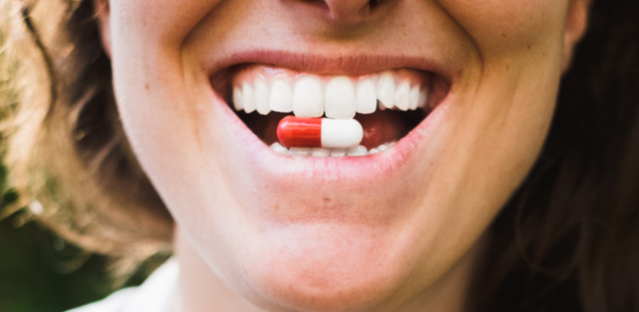 Mulher sorrindo com pílula antibiótica de terramicina entre os dentes.