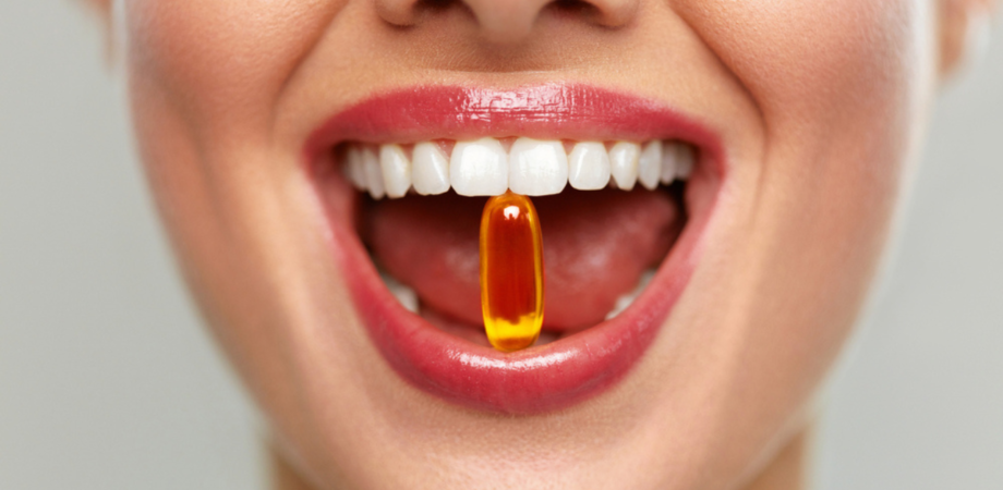 Uma boca com pílula de vitamina k2 entre os dentes.